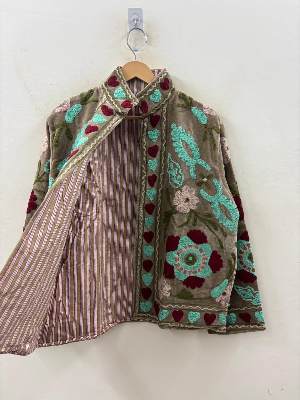 Handcrafted jacket with floral patterns and hearts on a wooden hanger against a white wall.