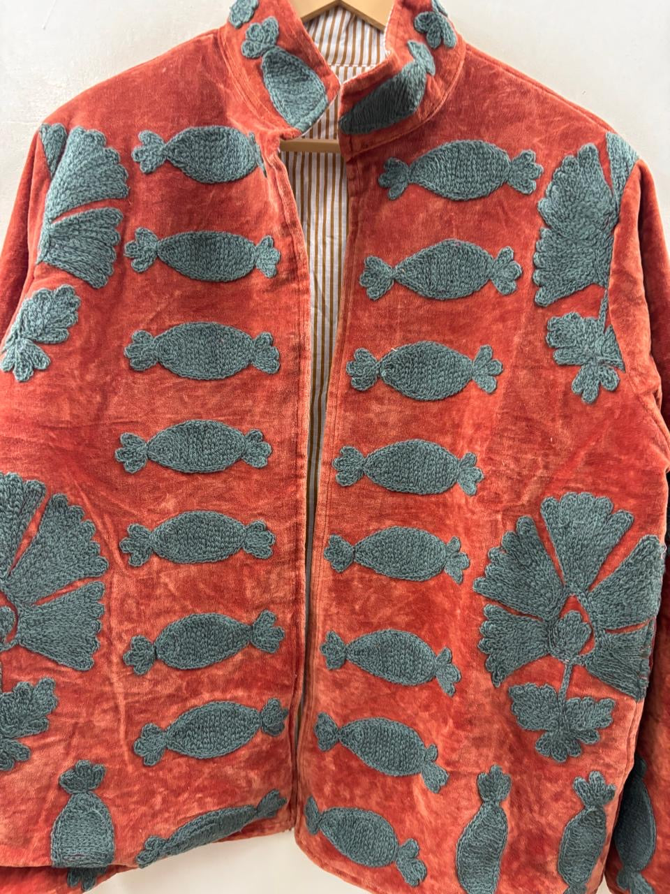 Red jacket with blue fish patterns on a hanger against a white background