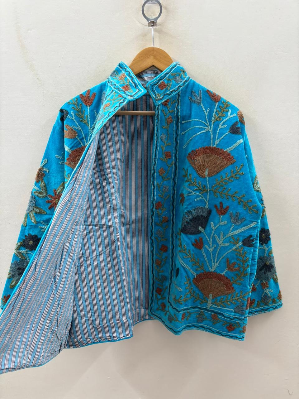 Blue embroidered jacket on a hanger against a white background