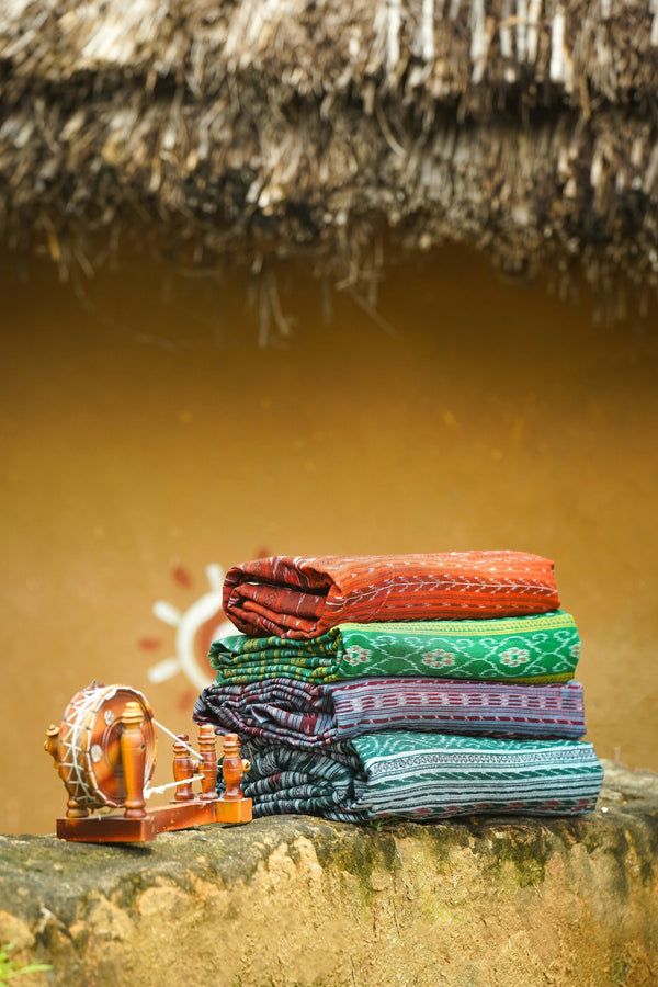 Stack of colorful fabric rolls on a stone surface with a thatched roof in the background
