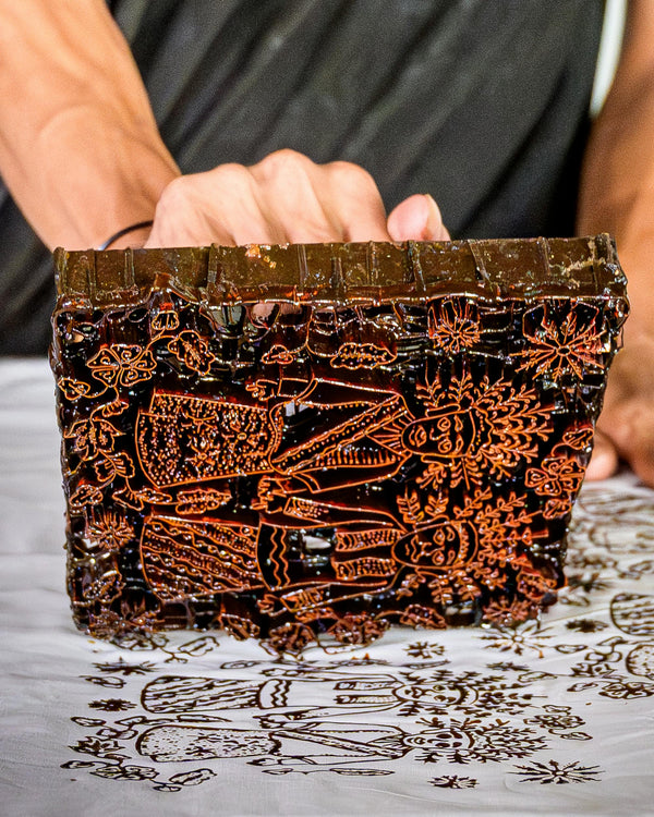 Hand holding a decorative wooden block with intricate carvings on a gray surface.