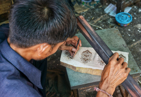 Man working on a piece of wood with intricate designs using tools.